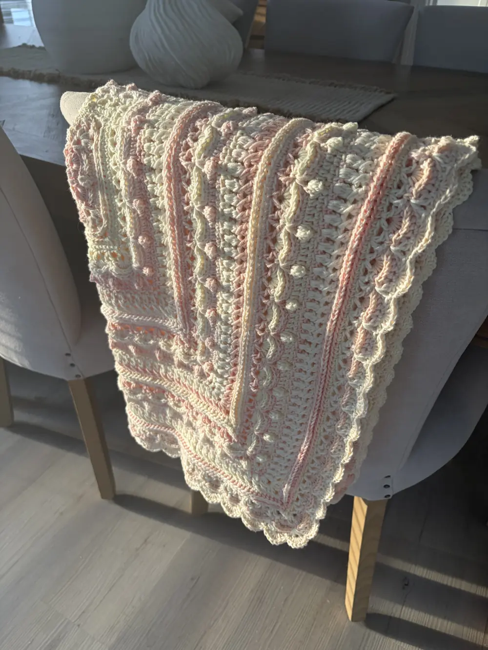 Cream and pink crocheted blanket with a scalloped edge, over a dining chair